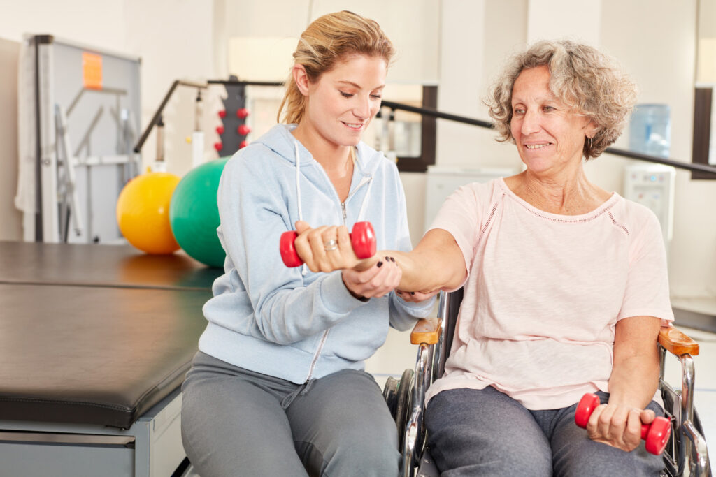 Physiotherapeutin hilft Senior Frau mit Handicap beim Reha Hanteltraining